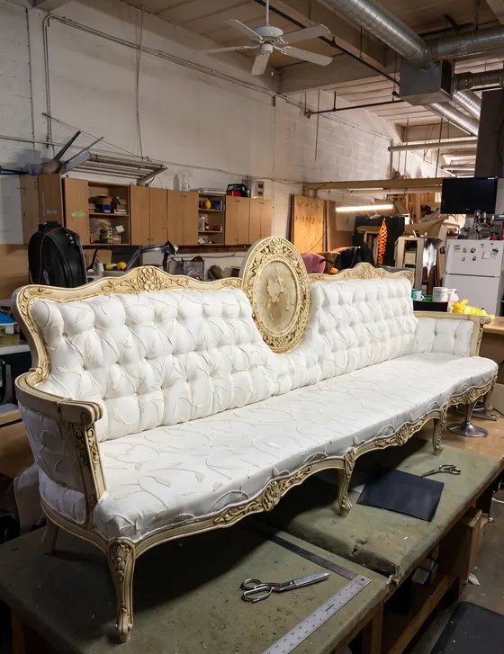 Sofá antiguo de madera dorada con capitoneado blanco