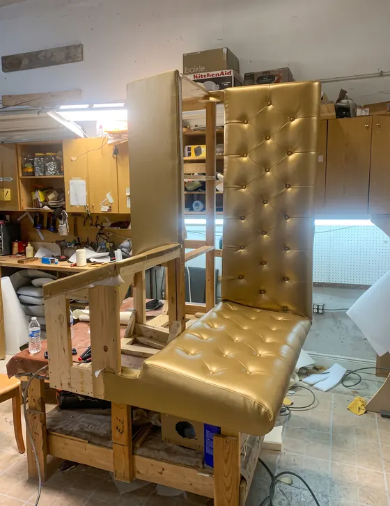 Sillón de respaldo alto capitoneado en dorado durante el tapizado
