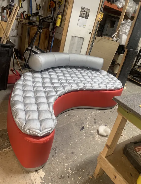 Sofá curvo de diseño con asiento plateado capitoneado y base roja